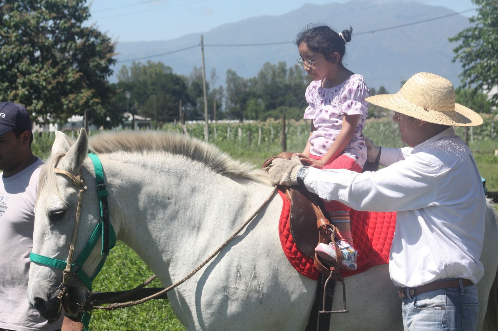 Una nena sonríe montada en un caballo blanco mientras un hombre la sostiene.