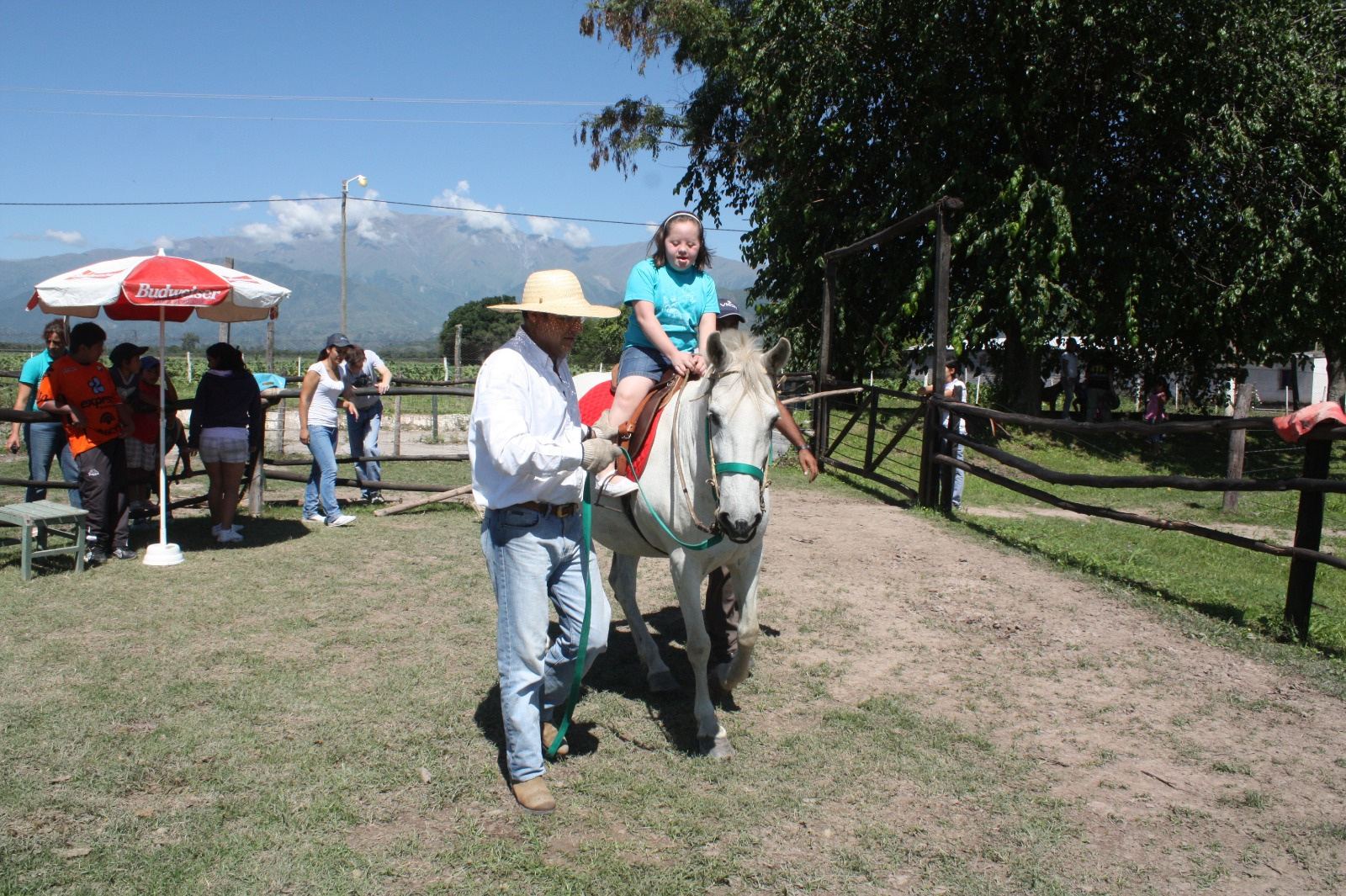 Una nena pasea a caballo guiada por un hombre con sombrero.