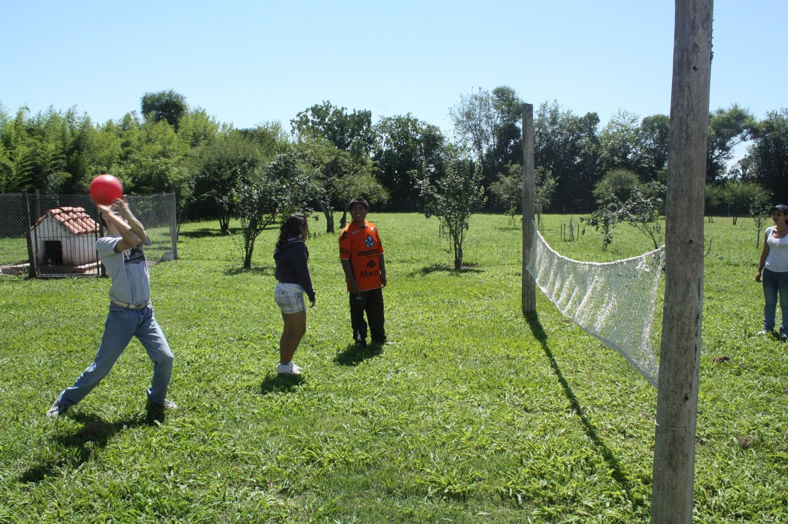 Un joven lanza una pelota roja en el parque mientras otros esperan.