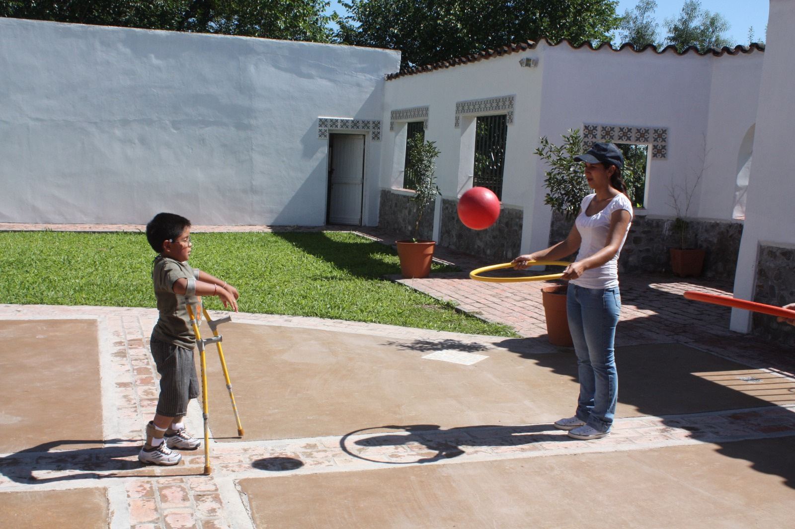 Un chico juega con un bastón en el patio mientras una profesional sostiene una pelota.