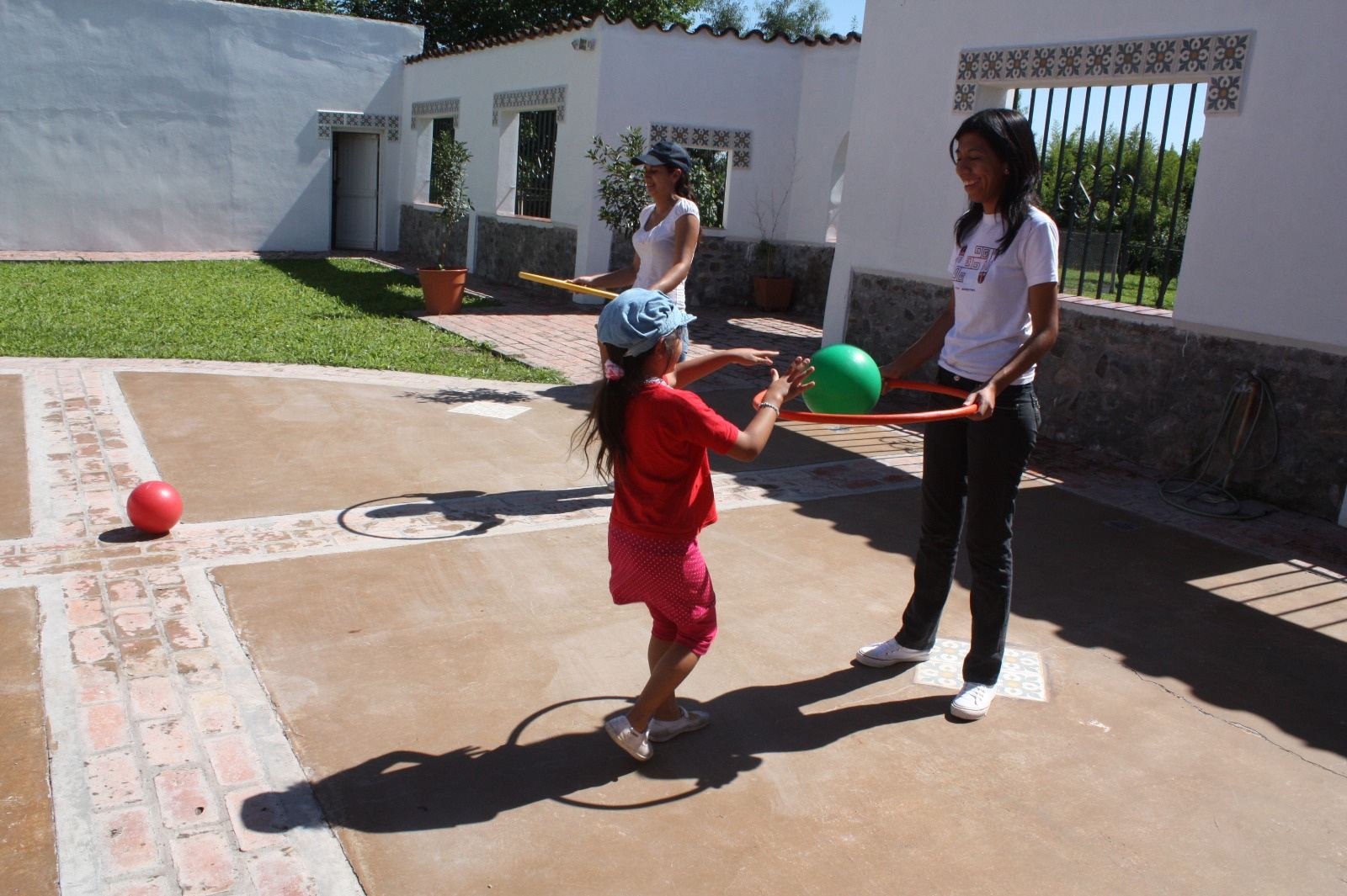 Una nena juega con una pelota y un aro junto a una profesional en el patio.